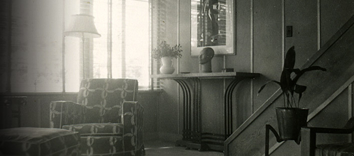 Northwest corner of the living room. We can see a staircase, a console table, artwork and a sofa near illuminated windows.