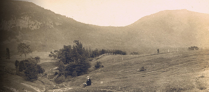 Early 20th century view of Mount St-Hilaire with a man sitting in a field in the foreground.