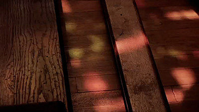 Scene from the video showing reflections of filtered light from a stained-glass window on a wooden church floor.