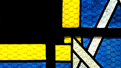 Scene from the video showing a detail of a circular stained-glass window made of abstract geometric shapes.