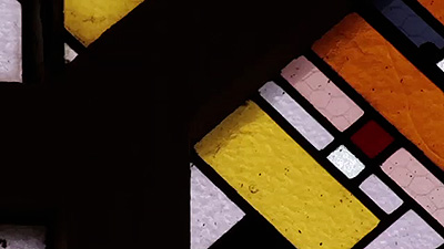 Scene from the video showing a stained-glass window composed of yellow, white, pink and black geometric shapes.