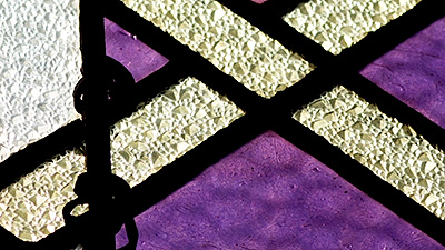 Scene from the video showing the detail of a stained-glass window composed of purple and white geometric shapes.