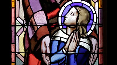 Scene from the video showing the detail of a stained-glass window representation of a praying child.