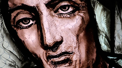Scene from the video showing the detail of a stained-glass window representation of a face.